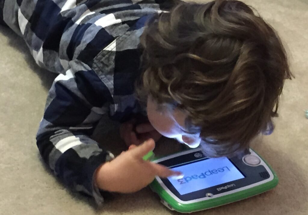 A child lying down using a tablet with a light on.