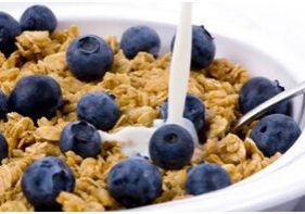 A bowl of cereal with blueberries and a spoon.