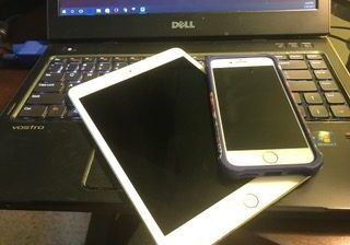 A white tablet and a smartphone on a Dell laptop keyboard.
